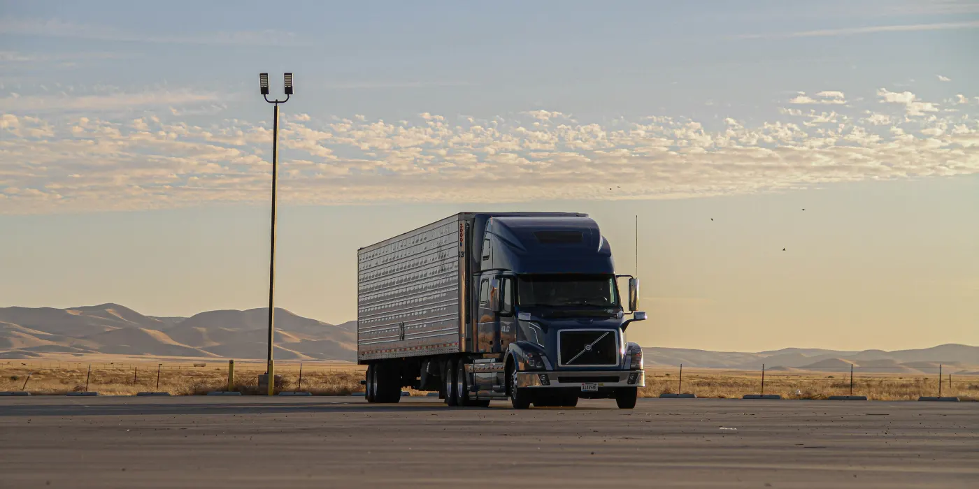 Blue semi tractor pulling a refrigerated trailer on a desert highway at dusk